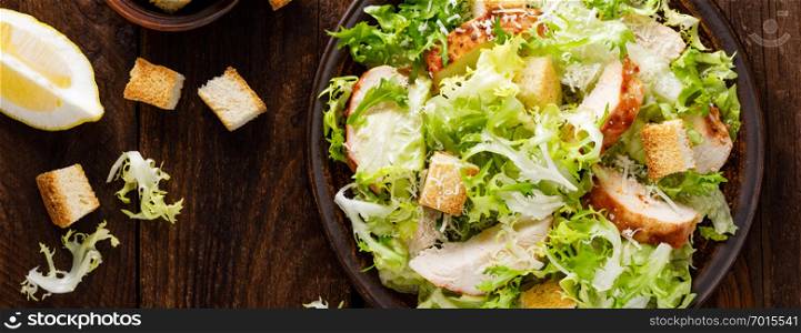 Caesar salad with grilled chicken meat, fresh lettuce, parmesan cheese and fried croutons. Classic North American cuisine. Top view. Banner