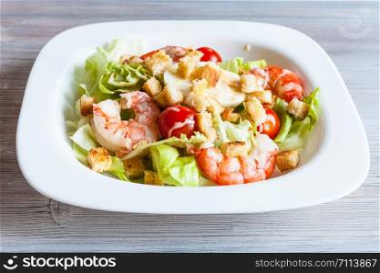 Caesar salad with prawns on white plate on gray wooden table