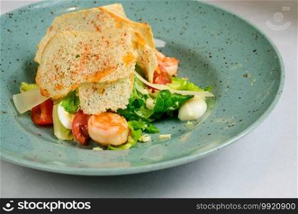Caesar salad with shrimp on blue plate on white background.Caesar salad with shrimps,top view. Caesar salad with shrimp on blue plate on white background