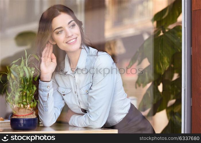 Cafe city lifestyle. Young woman sitting indoor in trendy urban cafe looking through the window. Cool young modern caucasian female model in her 20s