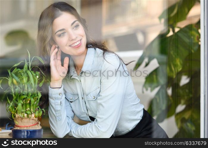 Cafe city lifestyle. Young woman smiling indoor in trendy urban cafe looking through the window. Cool young modern caucasian female model in her 20s