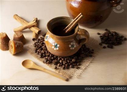 Cafe de Olla. Traditional Mexican coffee and basic ingredients for its preparation, coffee, cinnamon and piloncillo, served in a clay cup called  jarrito  on a rustic wooden surface.