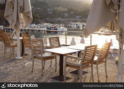 cafe on the waterfront. empty tables, chairs and a bay with boats in the background 