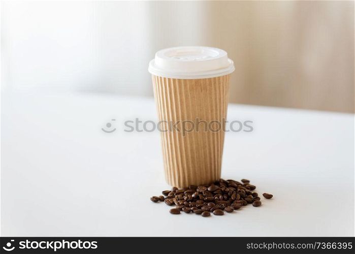 caffeine and takeaway drinks concept - close up paper cup and roasted coffee beans on white table. close up cup and roasted coffee beans on table