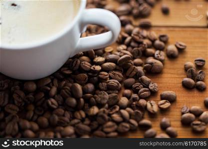 caffeine, objects and drinks concept - close up coffee cup and beans on wooden table