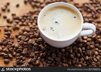 caffeine, objects and drinks concept - close up coffee cup and grains on wooden table