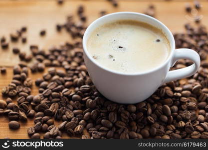 caffeine, objects and drinks concept - close up coffee cup and grains on wooden table