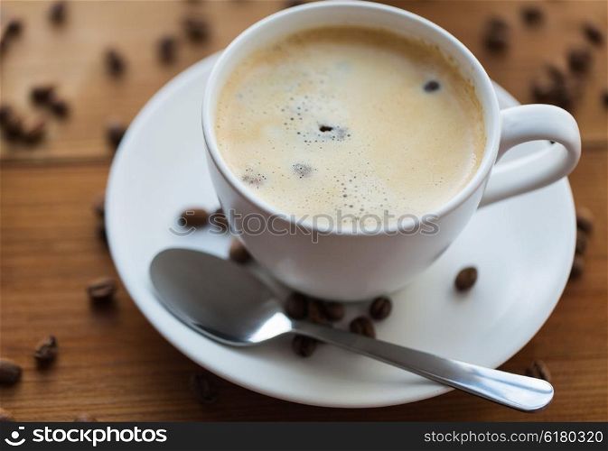 caffeine, objects and drinks concept - close up coffee cup and grains on wooden table