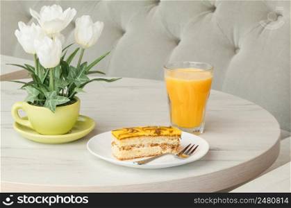 Cake and fork on a plate on a table with flowers on the background of the sofa. cake in a plate and a glass of juice on a table