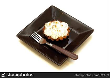 Cake basket with cream air lies on a brown plate with dessert fork