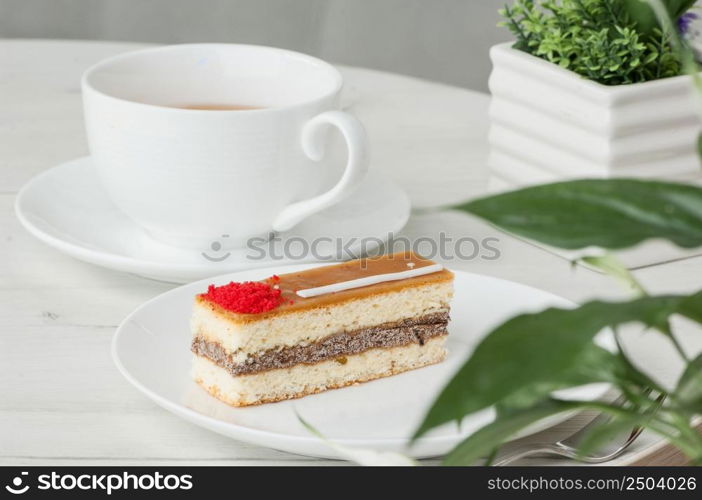 cake on a plate and a cup of coffee on a table with flowers. cake in a plate and a cup on the table