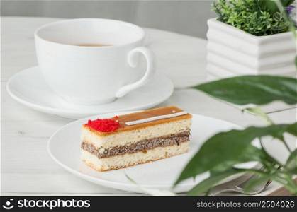 cake on a plate and a cup of coffee on a table with flowers. cake in a plate and a cup on the table
