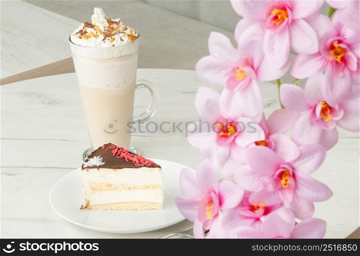 cake on a saucer and a cocktail in a tall glass on a table with flowers. cake in a plate and a glass of cocktail on a table