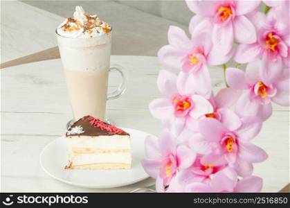 cake on a saucer and a cocktail in a tall glass on a table with flowers. cake in a plate and a glass of cocktail on a table