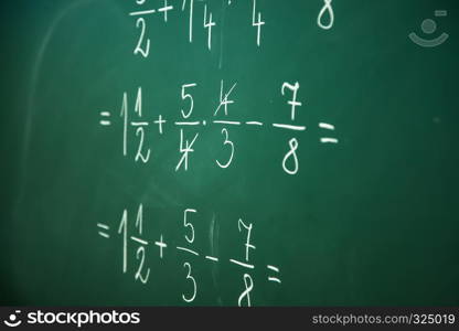 Calcualting with fractions on green blackboard at primary school