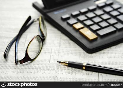 Calculator and glasses and pen on top of financial newspaper