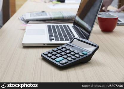 calculator, laptop computer, newspaper, document, pen and red coffee cup on wooden table for working concept