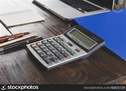 calculator, laptop computer, pen and notepad on wooden office desk