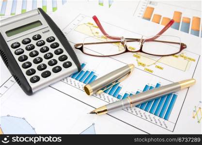 calculator, pen and glasses on business charts