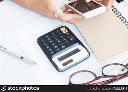 Calculator with bill slips on wooden table with woman hand using mobile phone, Business and finance