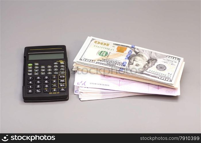 Calculator with dollar and euro notes on gray background