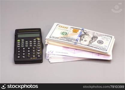 Calculator with dollar and euro notes on gray background