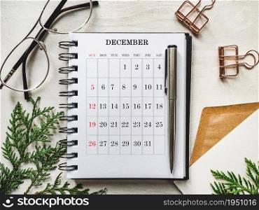Calendar and green branches of a Christmas tree lying on a white table. View from above, closeup, no people. Concept of preparation for a holiday. Congratulations for relatives, friends and colleagues. Calendar and green branches of a Christmas tree
