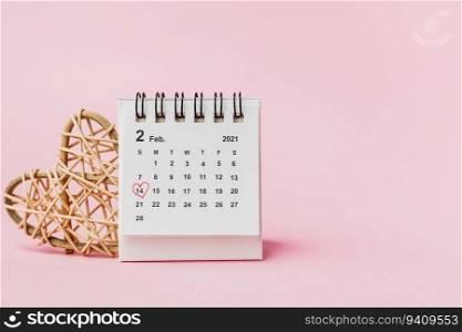 Calendar with red heart shaped marking on date February, 14 and wooden wicker heart against pink background for Valentine&rsquo;s day and love concept