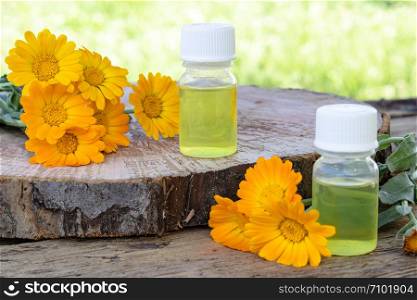calendula essential oil near the yellow flowers of calendula on a wooden background in nature. Extract of tincture of calendula. Medicinal plants. calendula essential oil near the yellow flowers of calendula on a wooden background in nature. Extract of tincture of calendula.