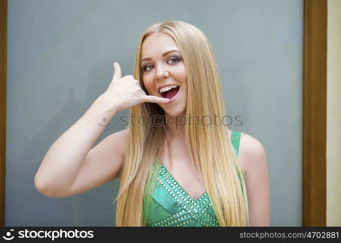 Call Me. Beautiful happy woman in green dress making a call me gesture, indoor