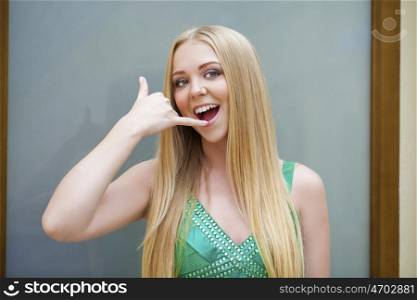Call Me. Beautiful happy woman in green dress making a call me gesture, indoor