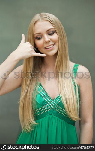 Call Me. Beautiful happy woman in green dress making a call me gesture, indoor