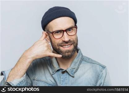 Call me please! Happy handsome man holds hand near ear, imitates mobile phone conversation, smiles joyfully, waits for call from someone, isolated over grey studio background. Communication concept
