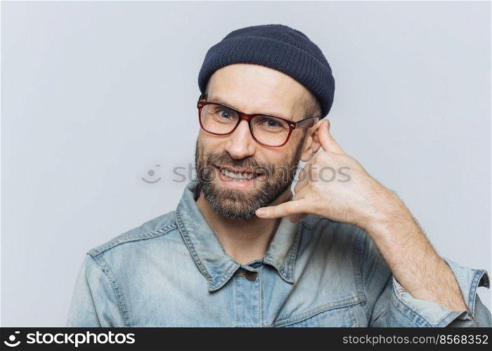 Call me please  Happy handsome man holds hand near ear, imitates mobile phone conversation, smiles joyfully, waits for call from someone, isolated over grey studio background. Communication concept