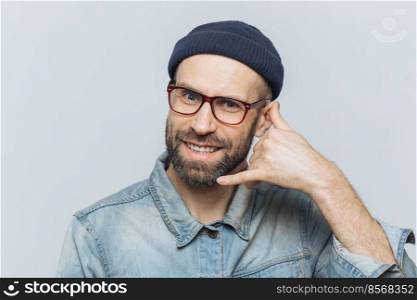 Call me please  Happy handsome man holds hand near ear, imitates mobile phone conversation, smiles joyfully, waits for call from someone, isolated over grey studio background. Communication concept
