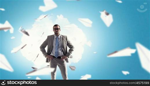 Calm and careless. Young businessman with hands on waist and paper planes flying around