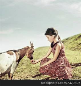 Calm and cheerful girl feeding a goat