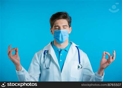 Calm doctor in mask relaxing, meditating. Man calms down, breathes deeply with mudra om on blue studio background. High quality photo. Calm doctor in mask relaxing, meditating. Man calms down, breathes deeply with mudra om on blue studio background.