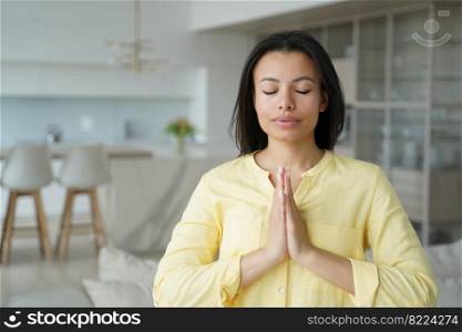 Calm female meditating standing at home with eyes closed put hands together in prayer, mindful woman makes namaste yoga gesture to keep calmness. Healthy lifestyle, meditation, stress relief concept.. Female makes namaste yoga gesture, keeping calmness, praying at home. Meditation, stress relief