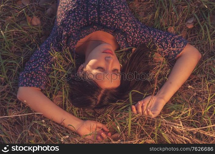 Calm girl in lying in tall grass in the fields with both hands behind her head