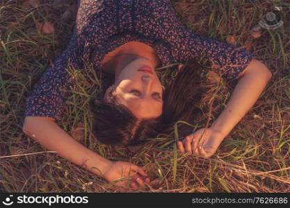 Calm girl in lying in tall grass in the fields with both hands behind her head