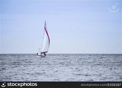 Calm image of sailing boat in soft blue sky with red sail detail