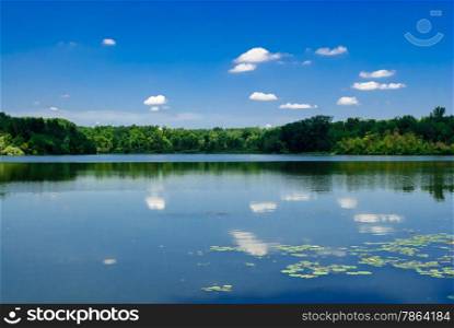Calm lake against reflected forest and blue sky with clouds
