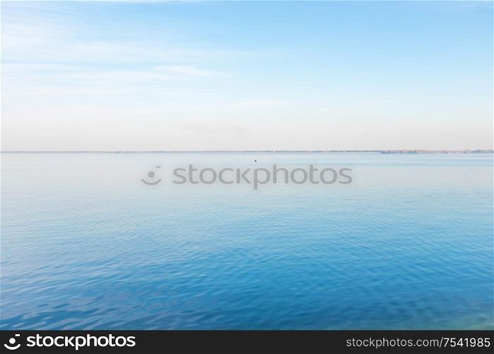 Calm landscape of sea water with fisher man in boat and a coast on horizon