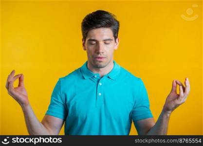 Calm man in blue relaxing, meditating. He calms down, breathes deeply with mudra om on yellow studio background. Yoga concept. Calm man in blue relaxing, meditating. He calms down, breathes deeply with mudra om on yellow studio background. Yoga concept.