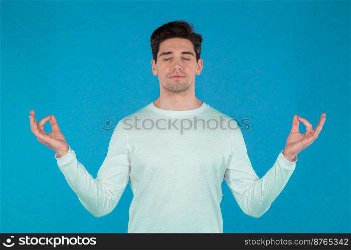 Calm man in white wear relaxing, meditating. He calms down, breathes deeply with mudra om on blue studio background. Yoga concept. High quality photo. Calm man in white wear relaxing, meditating. He calms down, breathes deeply with mudra om on blue studio background. Yoga concept.