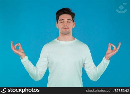 Calm man in white wear relaxing, meditating. He calms down, breathes deeply with mudra om on blue studio background. Yoga concept. High quality photo. Calm man in white wear relaxing, meditating. He calms down, breathes deeply with mudra om on blue studio background. Yoga concept.