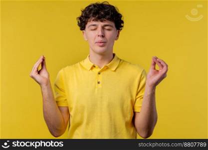 Calm man relaxing, meditating, refuses stress. Curly haired guy breathes deeply, calms down yellow studio background. Yoga, moral balance, zen concept. High quality photo. Calm man relaxing, meditating, refuses stress. Curly haired guy breathes deeply, calms down yellow studio background. Yoga, moral balance, zen concept.