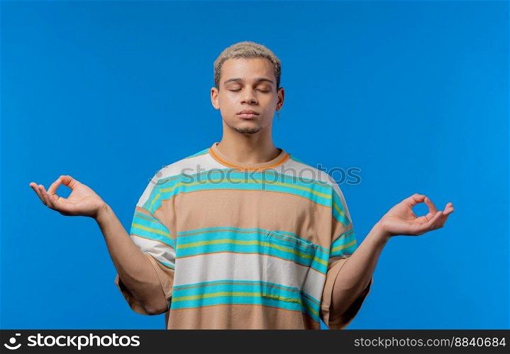 Calm man relaxing, meditating, refuses stress. Curly haired guy breathes deeply, calms down blue studio background. Yoga, moral balance, zen concept. High quality photo. Calm man relaxing, meditating, refuses stress. Curly haired guy breathes deeply, calms down blue studio background. Yoga, moral balance, zen concept.