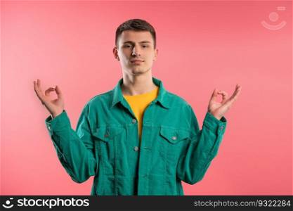 Calm man relaxing, meditating, refuses stress. Curly haired guy breathes deeply, calms down pink studio background. Yoga, moral balance, zen concept. High quality. Calm teen guy relaxing, meditating, refuses stress. Breathes deeply on pink